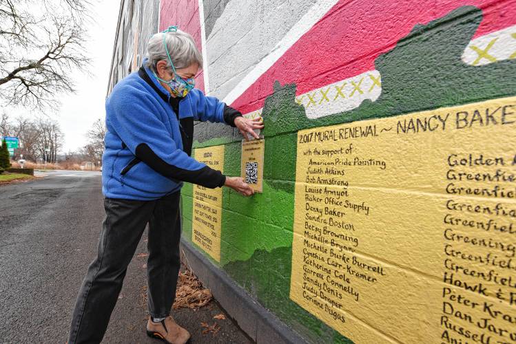 Nancy Baker hangs a QR code on the mural she created at Veterans Mall in Greenfield.